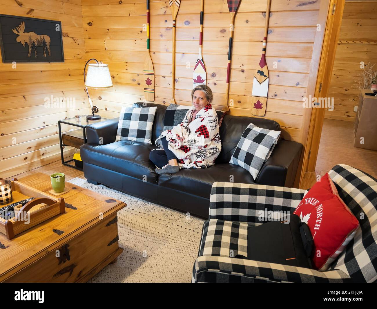 Porträt einer kaukasischen Frau mittleren Erwachsenen in Decke gehüllt entspannen auf dem Sofa in Blockhütte, während Urlaub im Winter genießen Stockfoto