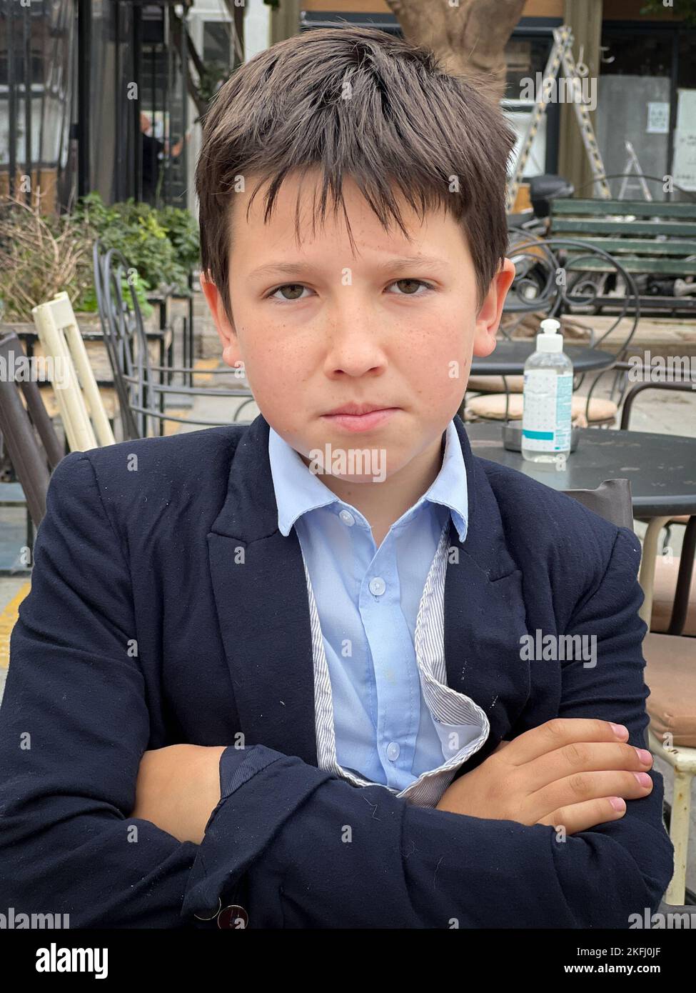 Nahaufnahme eines ernsthaften kaukasischen Jungen in Anzug mit gekreuzten Armen, der im Restaurant auf dem Bürgersteig sitzt Stockfoto