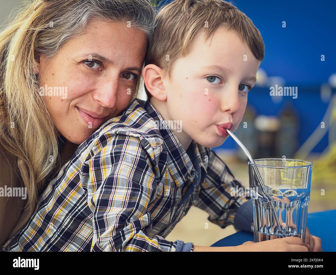 Nahaufnahme eines lächelnden kaukasischen Muttergesichts auf dem Rücken eines niedlichen Sohnes, der Wasser durch Stroh trinkt Stockfoto