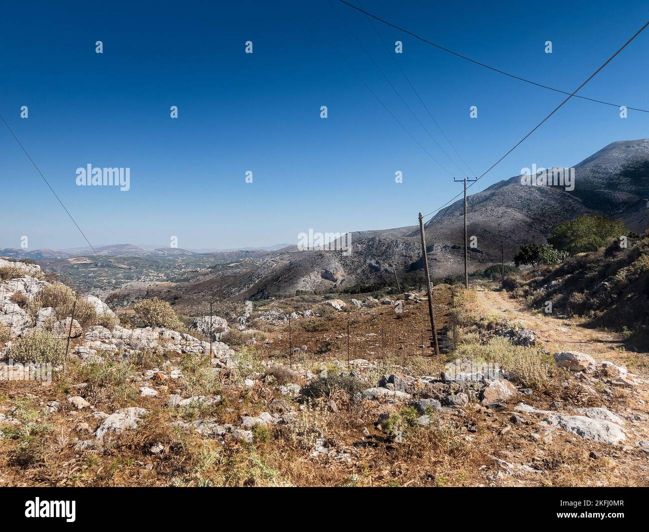 Stromleitungen inmitten wilder Pflanzen in der Landschaft gegen Berge und klaren blauen Himmel an sonnigen Tagen Stockfoto