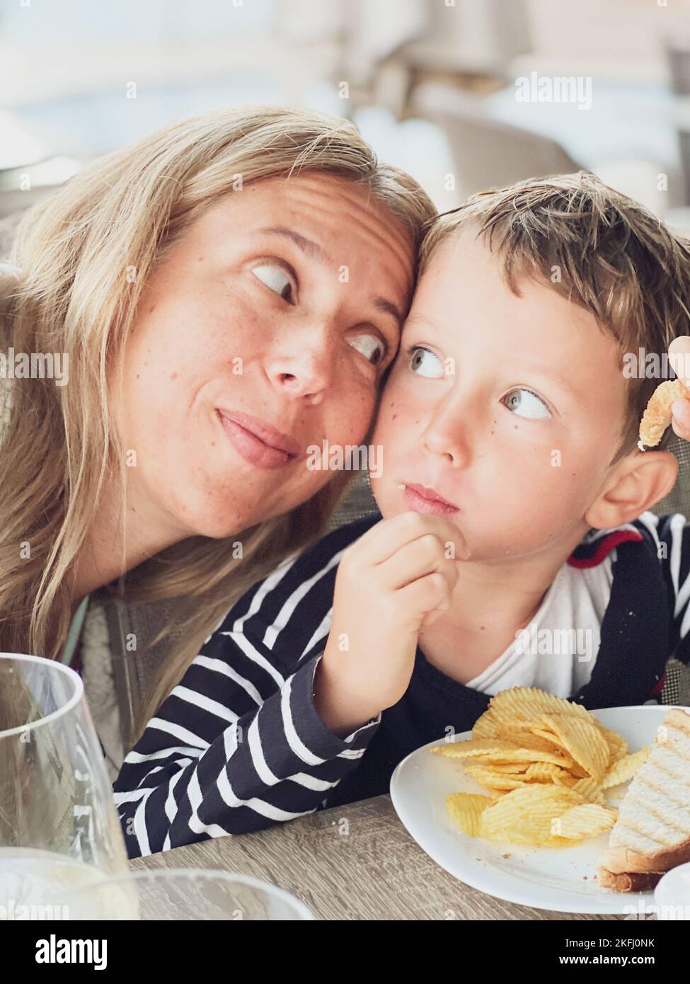 Nahaufnahme einer lächelnden Frau sieht den Sohn beim Essen eines süßen Jungen, der Sandwich und Chips auf dem Tisch im Restaurant isst Stockfoto