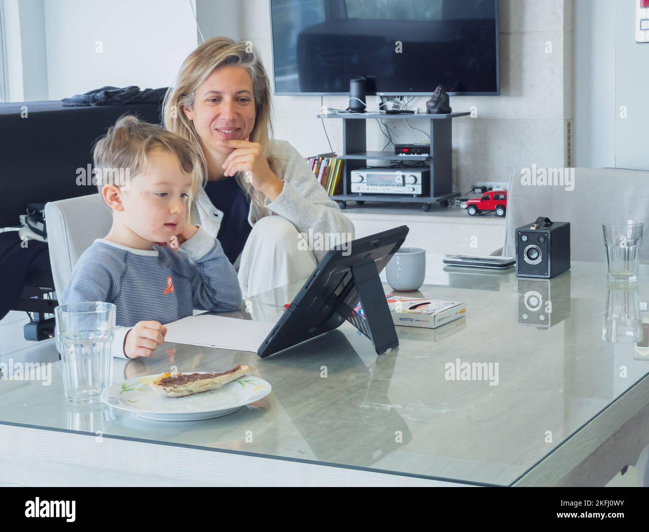 Lächelnde Mutter mit mittlerem Erwachsenen sitzt mit niedlichem Sohn e-Learning durch digitales Tablet auf dem Esstisch zu Hause Stockfoto