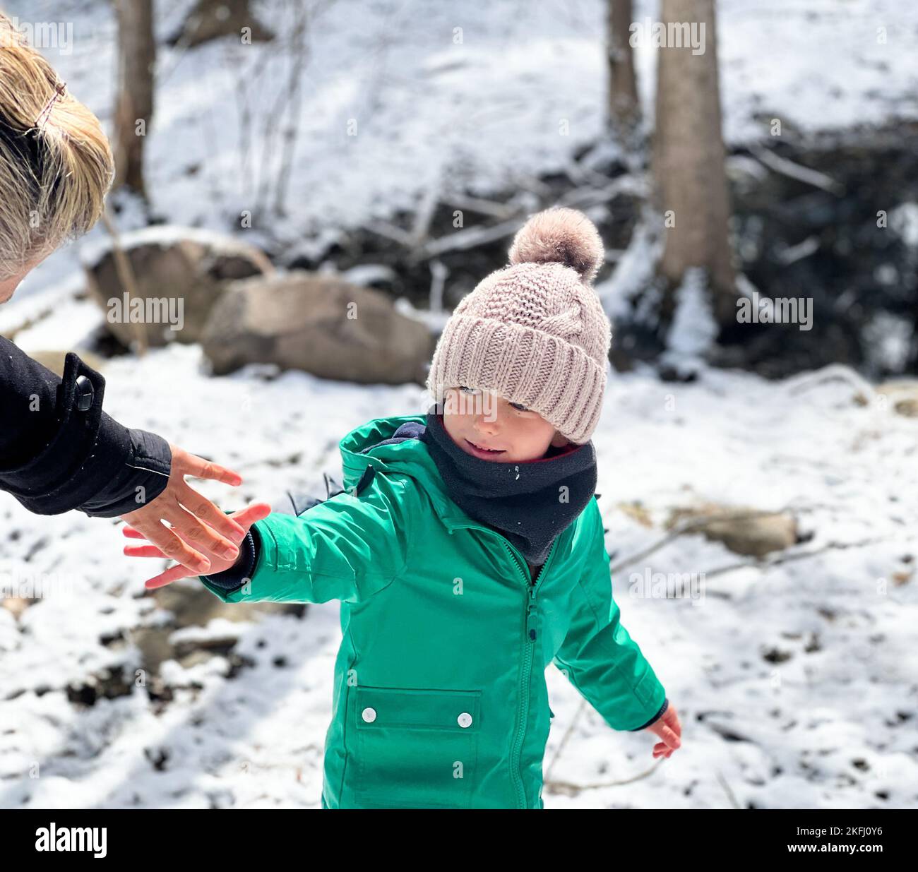 Junge in warmer Kleidung, die die Hand der Mutter hält, während er während des Urlaubs auf schneebedecktem Land im Wald steht Stockfoto
