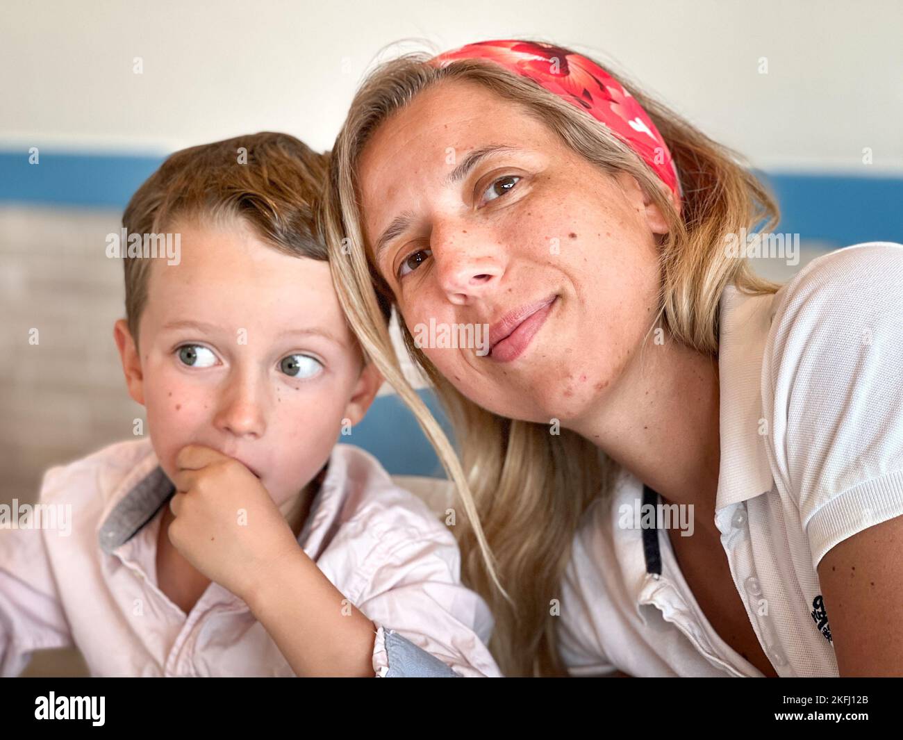 Porträt einer lächelnden Mutter, die sich auf den Kopf des Sohnes lehnt, an der Wand sitzt und zu Hause gemeinsam Freizeit verbringt Stockfoto
