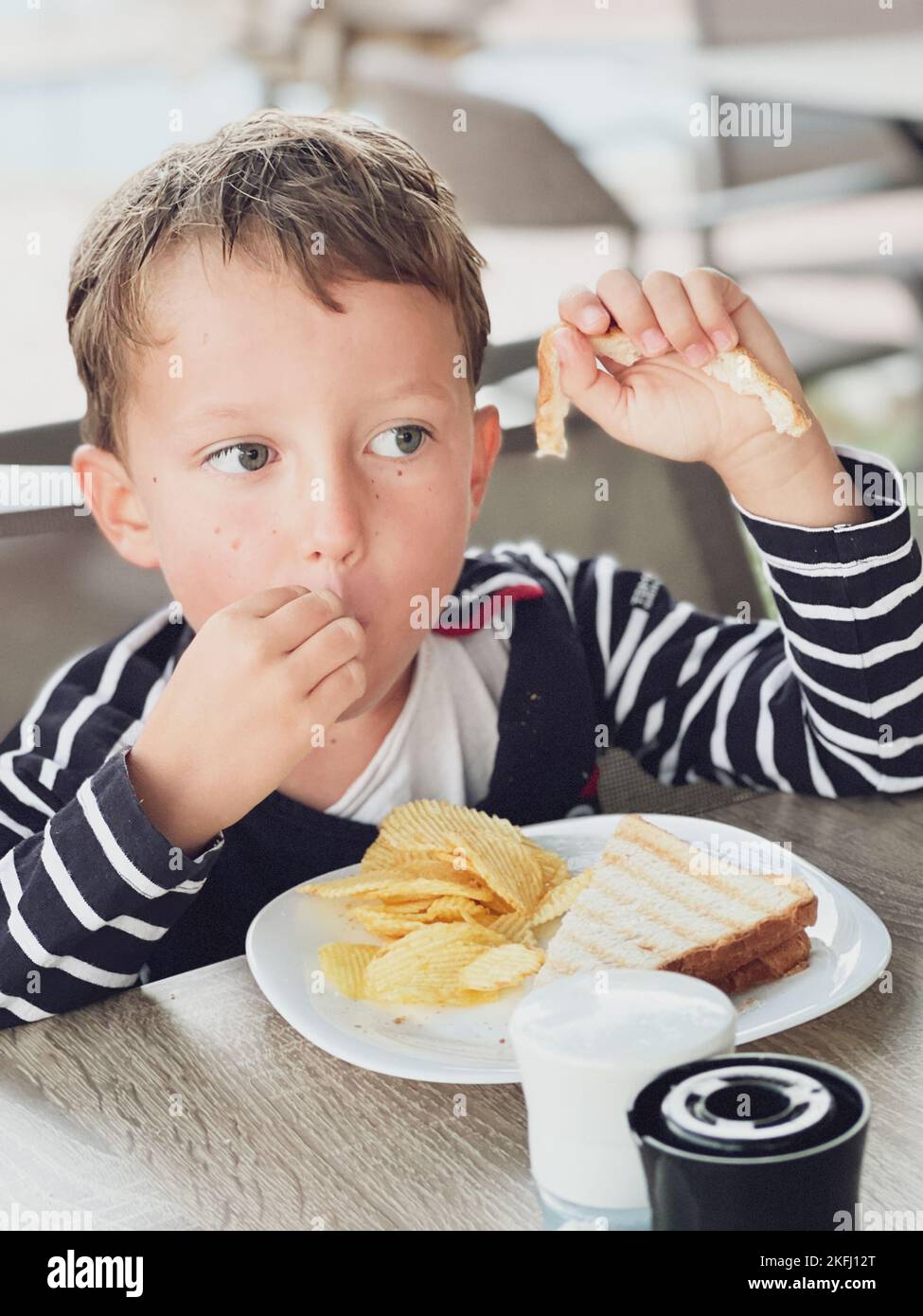Nahaufnahme eines niedlichen kaukasischen Jungen, der wegschaut, während er Sandwich und Chips auf dem Tisch im Restaurant isst Stockfoto