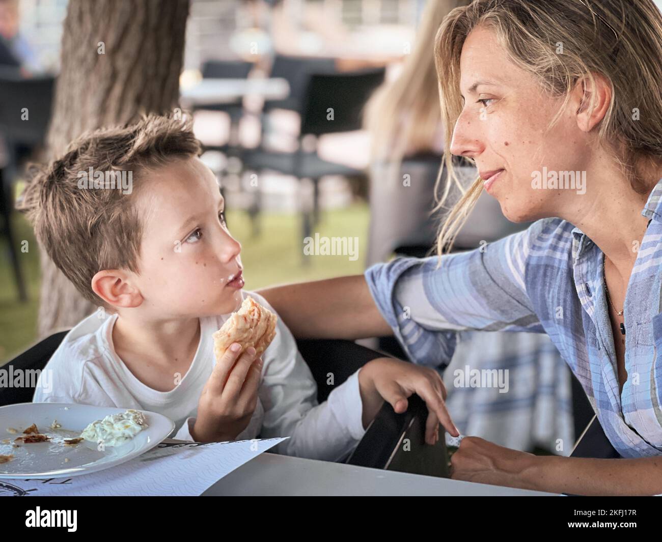 Kaukasische Mutter schaut auf niedlichen Sohn Sandwich essen, während auf Stuhl im Restaurant während des Wochenendes sitzen Stockfoto