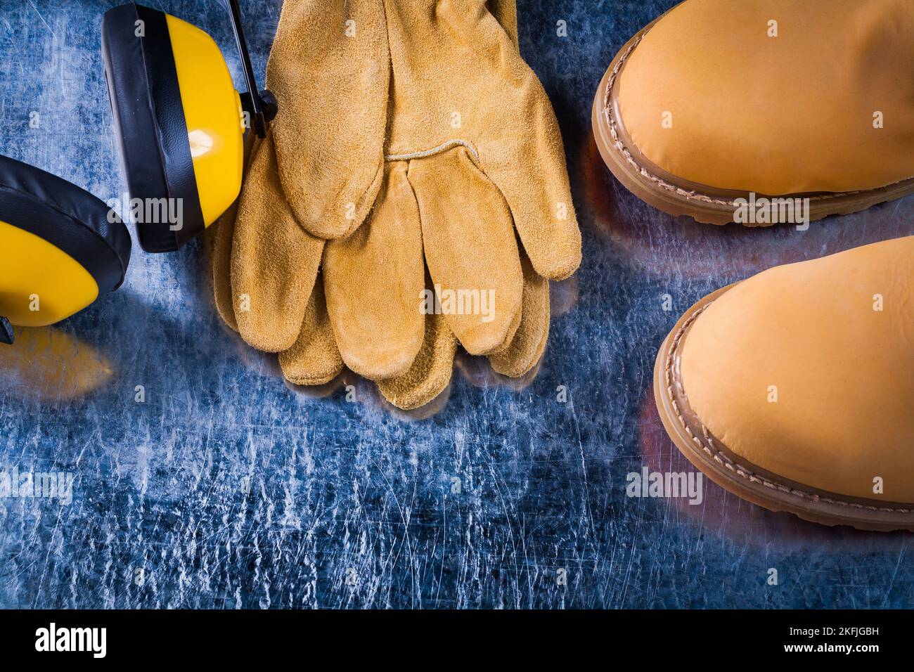 Sicherheitsstiefel Lederhandschuhe und Kopfhörer zur Geräuschreduzierung auf zerkratzter Metalloberfläche, horizontales Bildkonstruktionskonzept. Stockfoto