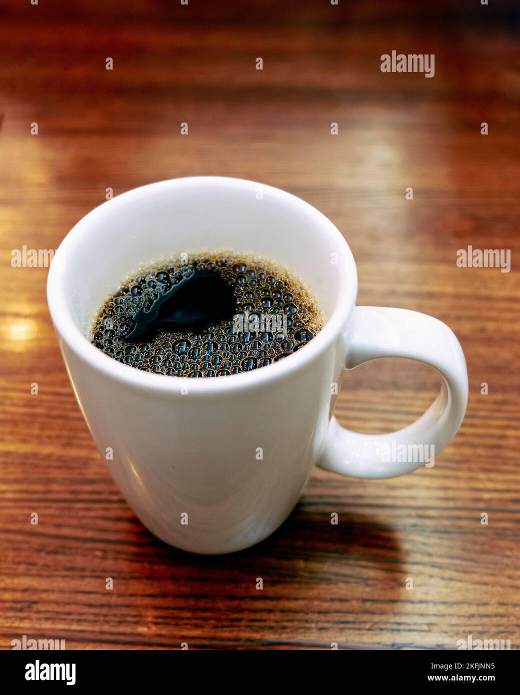 Große weiße Keramik-Kaffeetasse oder -Tasse mit heißem schwarzem Kaffee auf einem Restauranttisch. Stockfoto