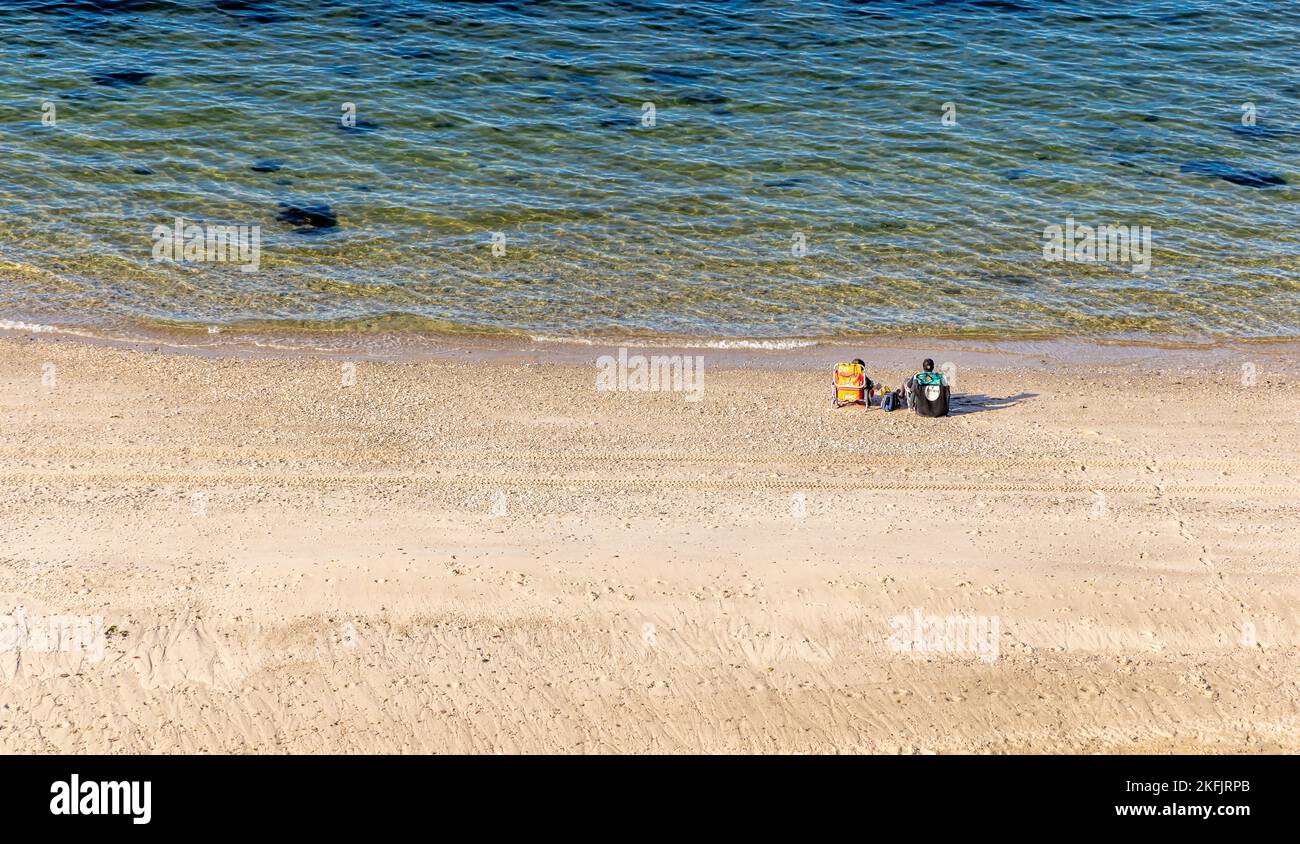 Ein Paar sitzt auf Liegen an einem großen Strand an der Nordküste Stockfoto