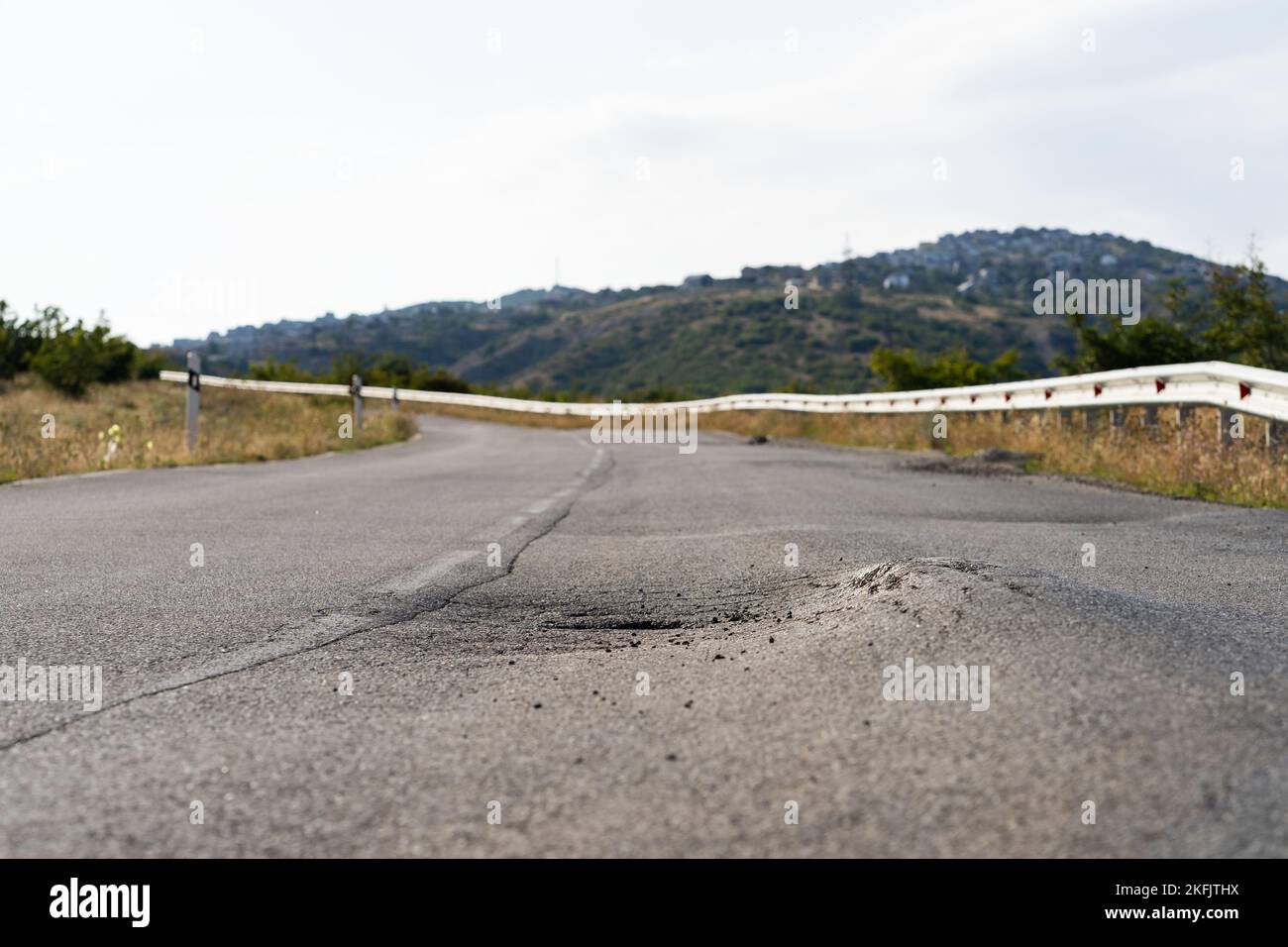 Gebrochener Fleck mitten auf einer Straße, die sich auf dem Land gegen hohe Waldberge und Hügel erstreckt Stockfoto