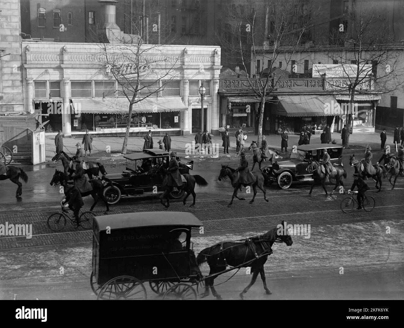 Childs Restaurant, Pennsylvania Avenue, Washington DC, 1917. Erster Weltkrieg: Zuschauer beobachten militärische Vorsteher, die die Kornege offizieller Autos begleiten. Der Heckwagen hat US- und deutsche Flaggen. Johann Heinrich von Bernstorff, deutscher Botschafter in den Vereinigten Staaten, verließ die USA am 3. Februar 1917, nachdem Präsident Woodrow Wilson die diplomatischen Beziehungen zu Deutschland abgebrochen hatte. Childs Restaurants war eine der ersten nationalen Speiseketten in den USA und Kanada. Auf der rechten Seite befinden sich Pressler Bros. Haberdaschers und die Büros von Gray Line Sightseeing Tours. Stockfoto