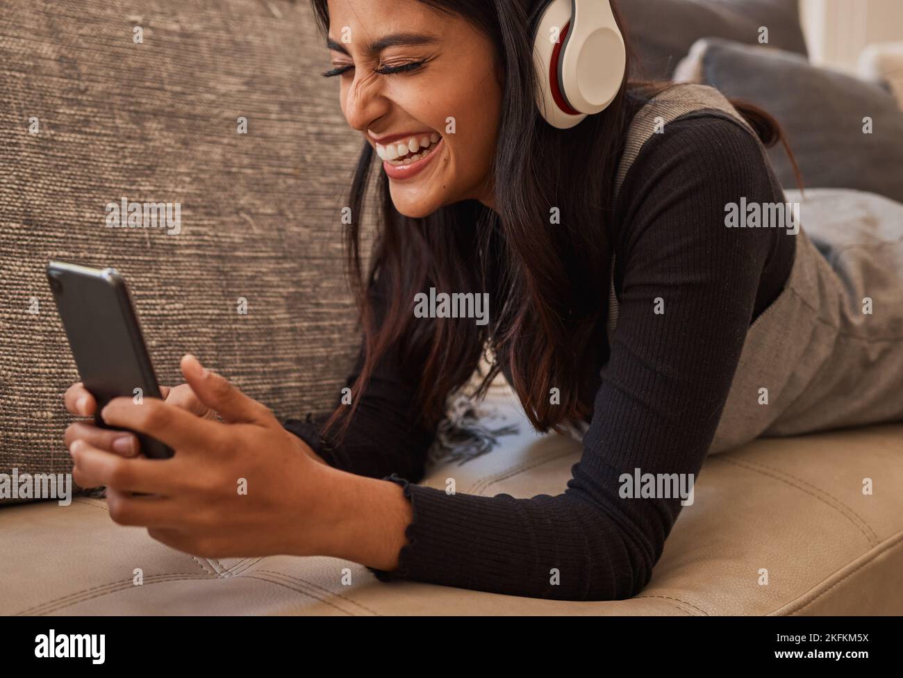 Smartphone, Kopfhörer und Frau auf dem Sofa hören Musik, sehen Online-Video-Chat oder Mobil-App-Zoom-Anruf. Aufgeregt, entspannen und Musik von einem jungen Mädchen Stockfoto