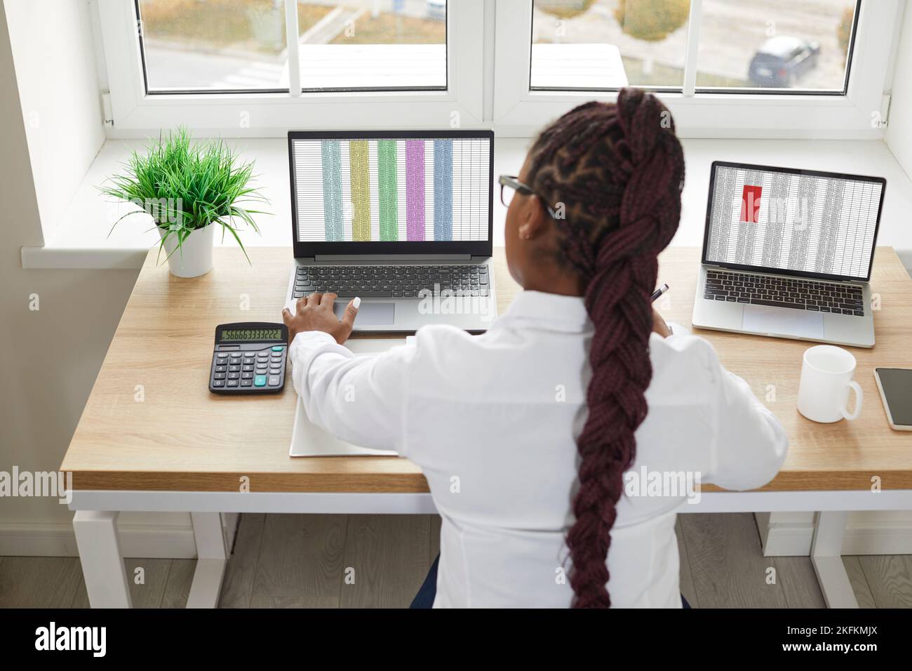 Rückansicht einer Buchhalterin, die an ihrem Schreibtisch sitzt und an zwei Laptops arbeitet Stockfoto