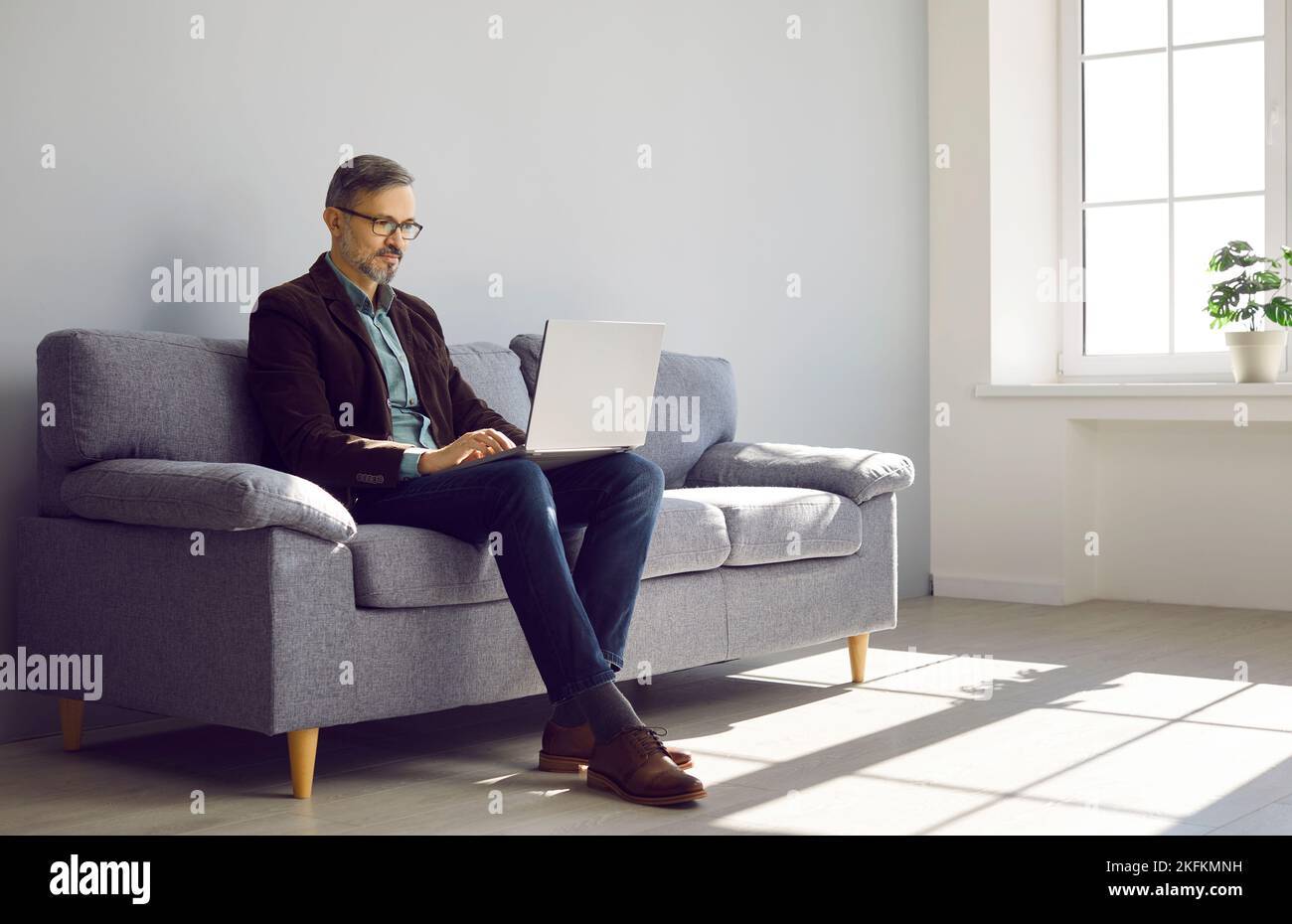 Erfolgreicher reifer Geschäftsmann sitzt auf der Couch und arbeitet an einem modernen Laptop-Computer Stockfoto