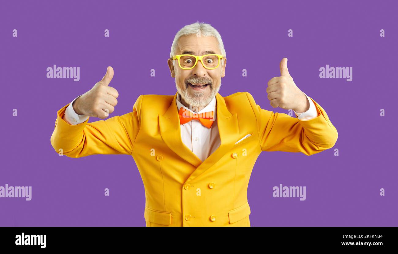 Fröhlicher, lustiger, charismatischer Seniorchef, der auf violettem Hintergrund die Daumen hochzeigt. Stockfoto