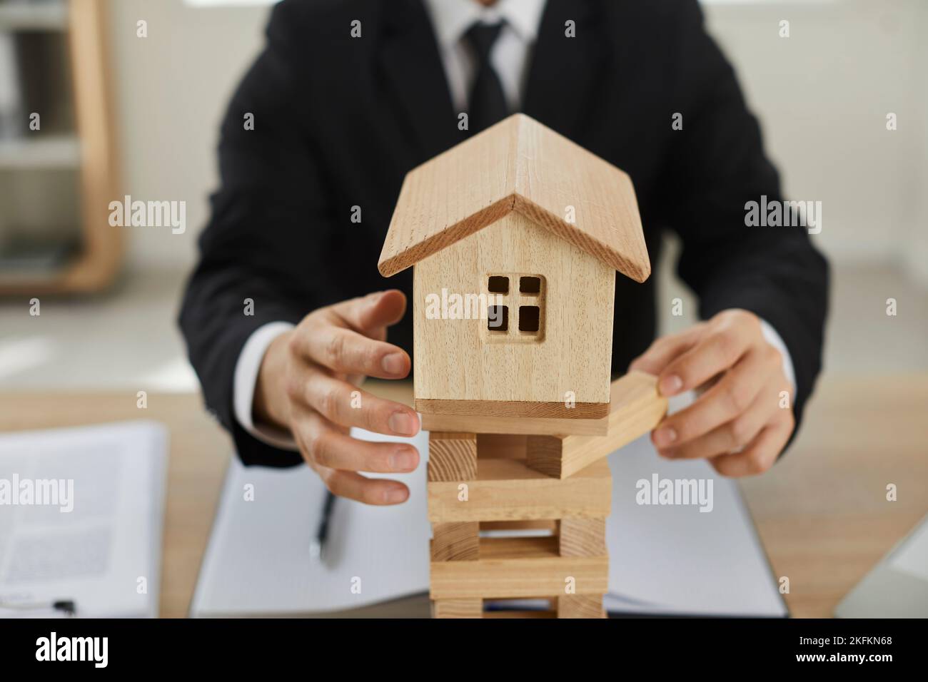 Der Mann entfernt Blöcke unter einem kleinen Holzhaus und demonstriert damit die Bedeutung der Hausversicherung. Stockfoto