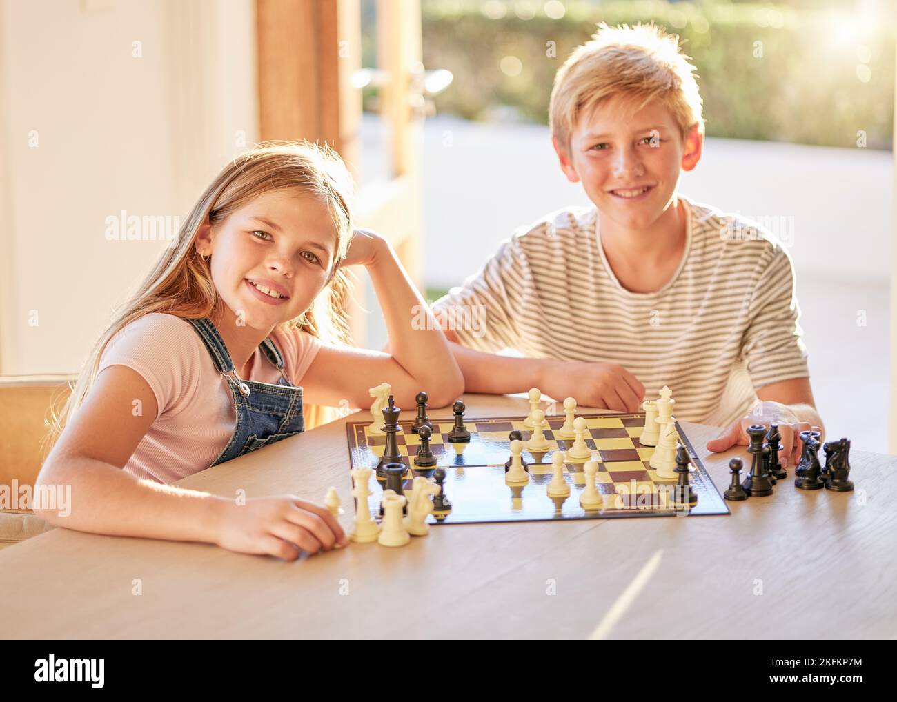 Portrait, Schach und Kinder entspannen sich an einem Tisch mit Brettspiel, Bindung und Lernen in einem Wohnzimmer in ihrem Zuhause. Kinder, Schachbrett und Gehirnaktivität Stockfoto
