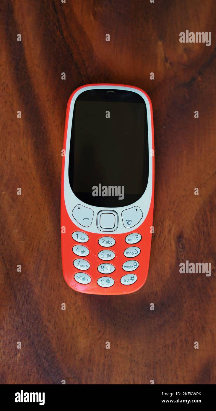 Ein Telefon mit Tastenfeld, dessen Tasten auf schwarzem Hintergrund isoliert sind. Altes Mobiltelefon mit schwarzem Display. Nahaufnahme eines orangefarbenen Mobils von 2g, 3G in Indien. Technologie und Stockfoto