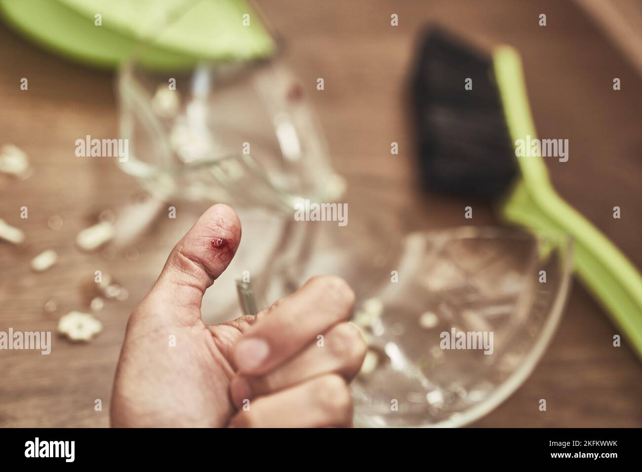 Nahaufnahme eines geschnittenen weiblichen Fingers auf dem Hintergrund einer geteilten Tasse und einer Bürste mit einer Kehrschaufel zum Reinigen. Eine Wunde mit Blut, die beim Reinigen von zerbrochenem Geschirr erhalten wurde. Hochwertige Fotos Stockfoto