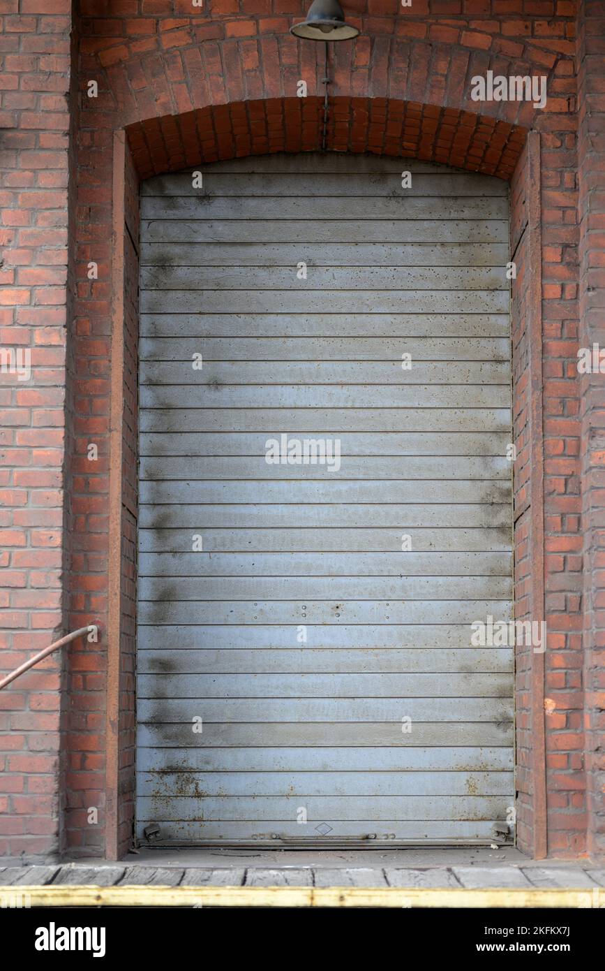 Graue Rollentür eines alten Gebäudes mit einer braunen Ziegelmauer Stockfoto