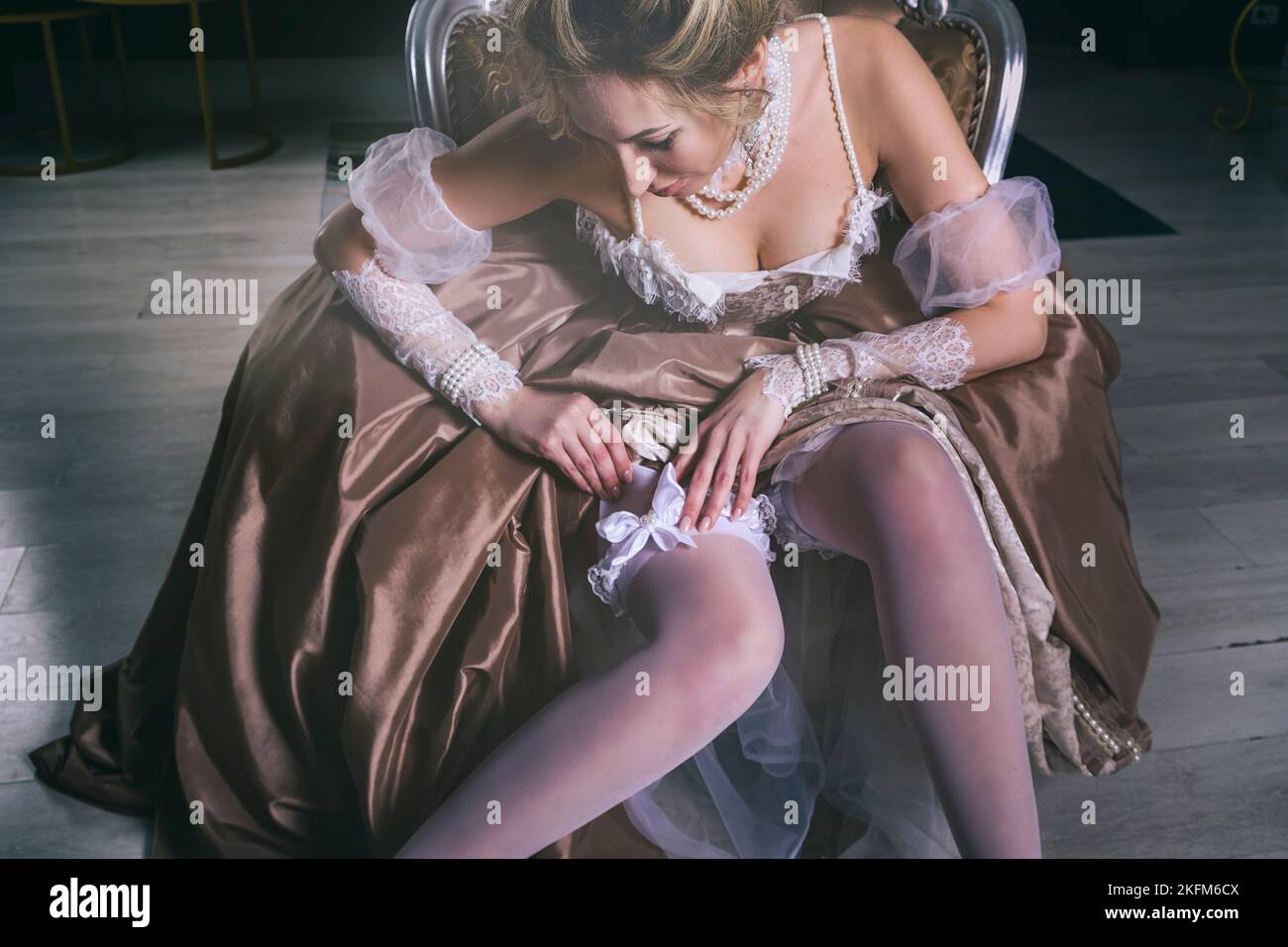 Eine junge Frau in einem Kleid aus dem 18.. Jahrhundert mit Spitze sitzt im Boudoir und passt den Verband an ihren Strümpfen an Stockfoto