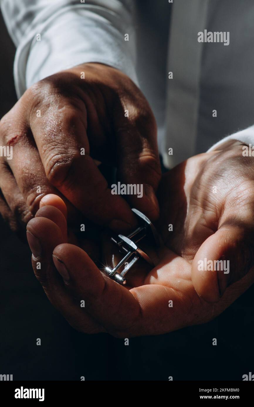 Hochzeitsmode für Männer. Nahaufnahme eines kaukasischen Mannes, der die Manschettenknöpfe in der Hand hält Stockfoto