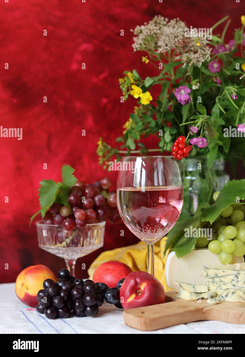 Wein, Käse, Obst und Blumen auf einem Tisch. Lebendige Farben frischer Beeren und Trauben. Farbenfrohes Stillleben mit einem Glas rosa Wein und Obst. Stockfoto