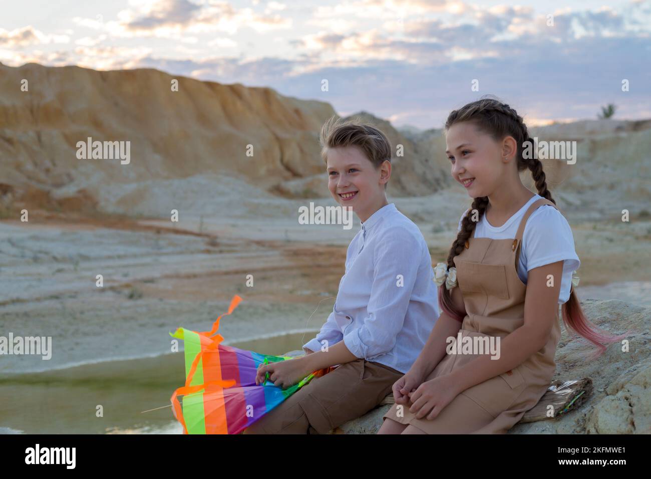 Ein Junge und ein Mädchen haben Spaß, am Fluss mit einem hellen gestreiften Drachen zu sitzen. Stockfoto