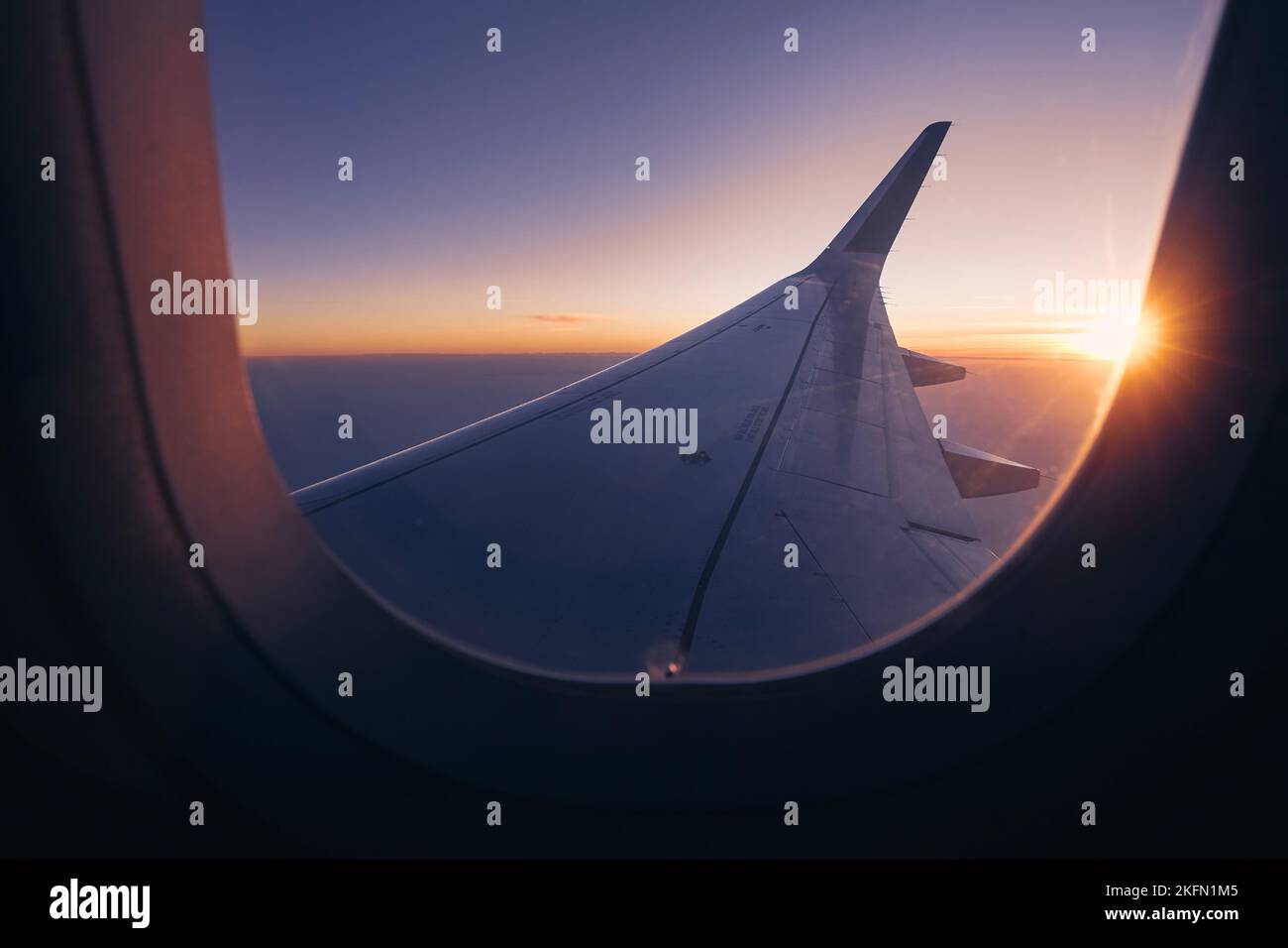 Romantischer Blick vom Flugzeugfenster über den Flügel während des wunderschönen Sonnenuntergangs. Die Sonne steht am Horizont und färbt den Himmel. Stockfoto