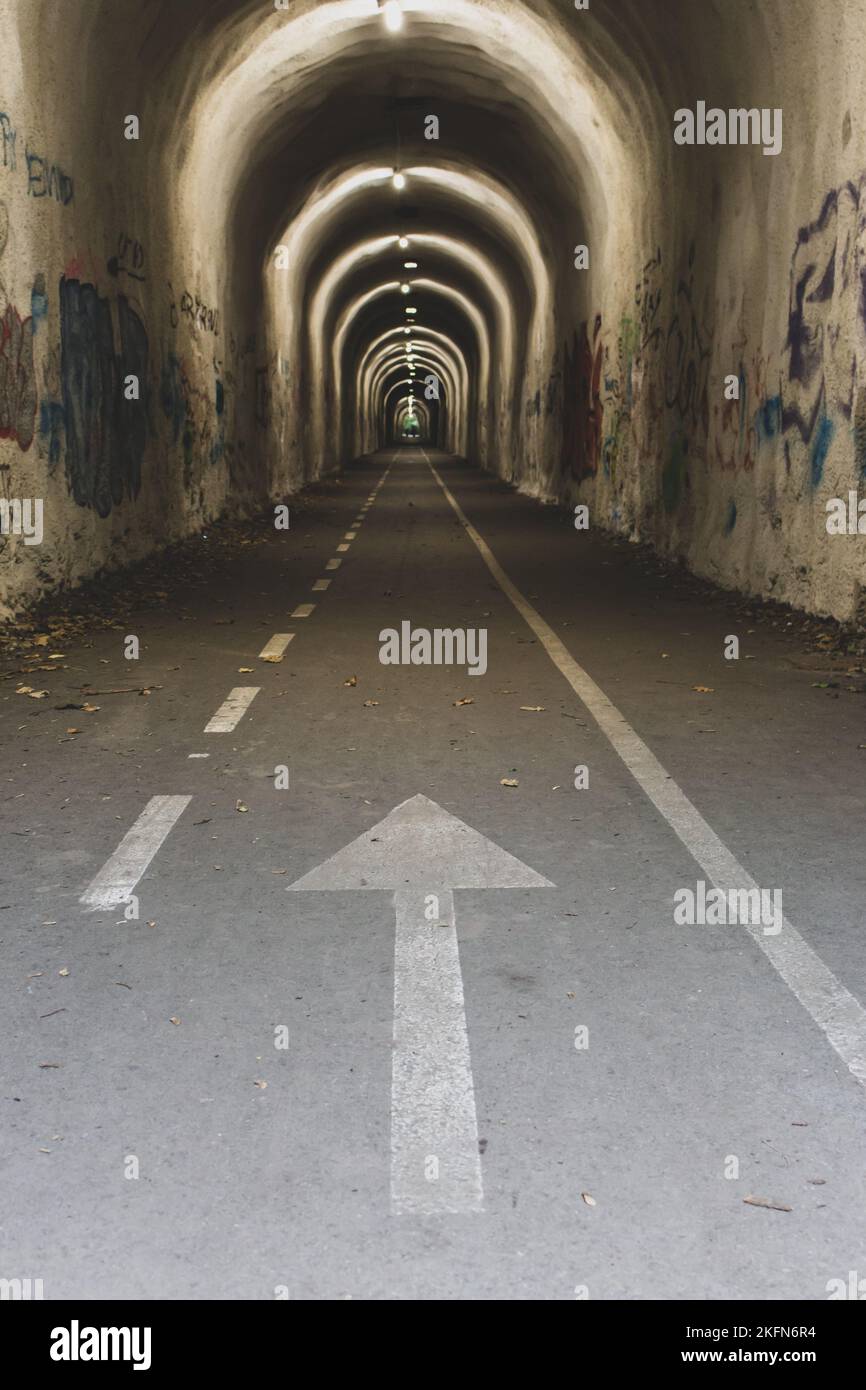 Enger Tunnel mit Pfeilschild. Leerer Tunnel mit Richtungszeichen. Konzept für Reiseziele. Eingang zum Tunnel auf dem Camino de Santiago. Stockfoto