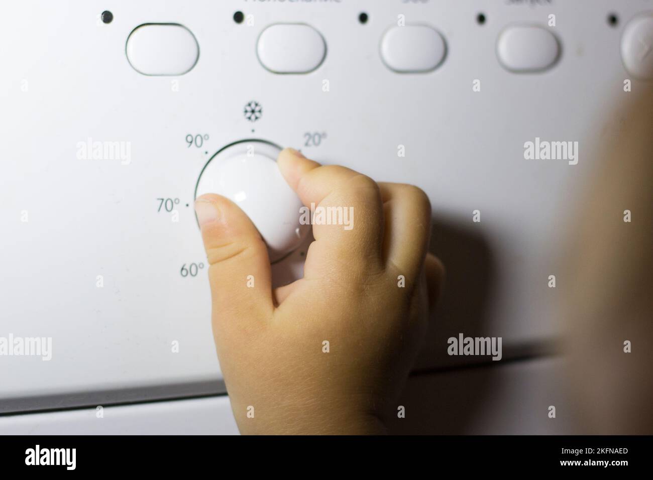Die Hand eines Kindes drückt einen Knopf an einer Waschmaschine Stockfoto