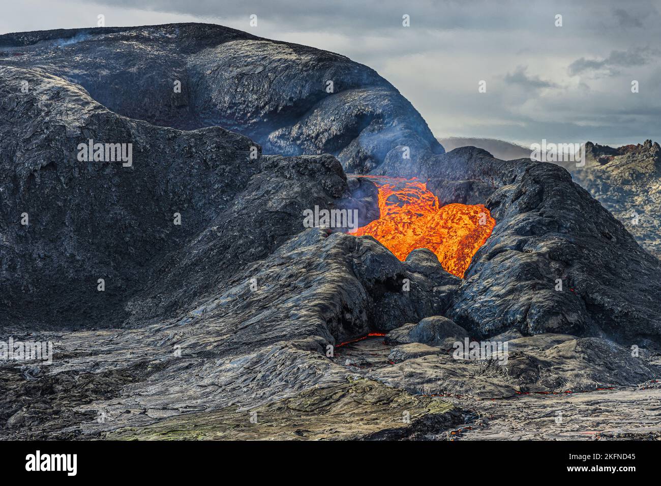 Sprudelnde Lava fließt aus einem aktiven vulkanischen Krater. Landschaft in Island auf der Halbinsel Reykjanes. Krater mit gekühltem und flüssigem Magmagestein. Wolken Stockfoto