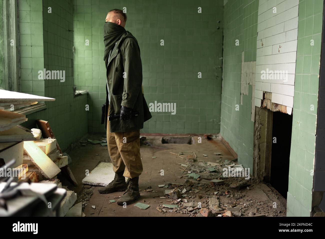 Der Mensch steht zwischen den Ruinen eines zerstörten Gebäudes und hält eine Waffe und eine Taschenlampe in den Händen. Das Konzept des Überlebenden nach dem Ende der Welt oder des dritten Weltkriegs ist es Stockfoto