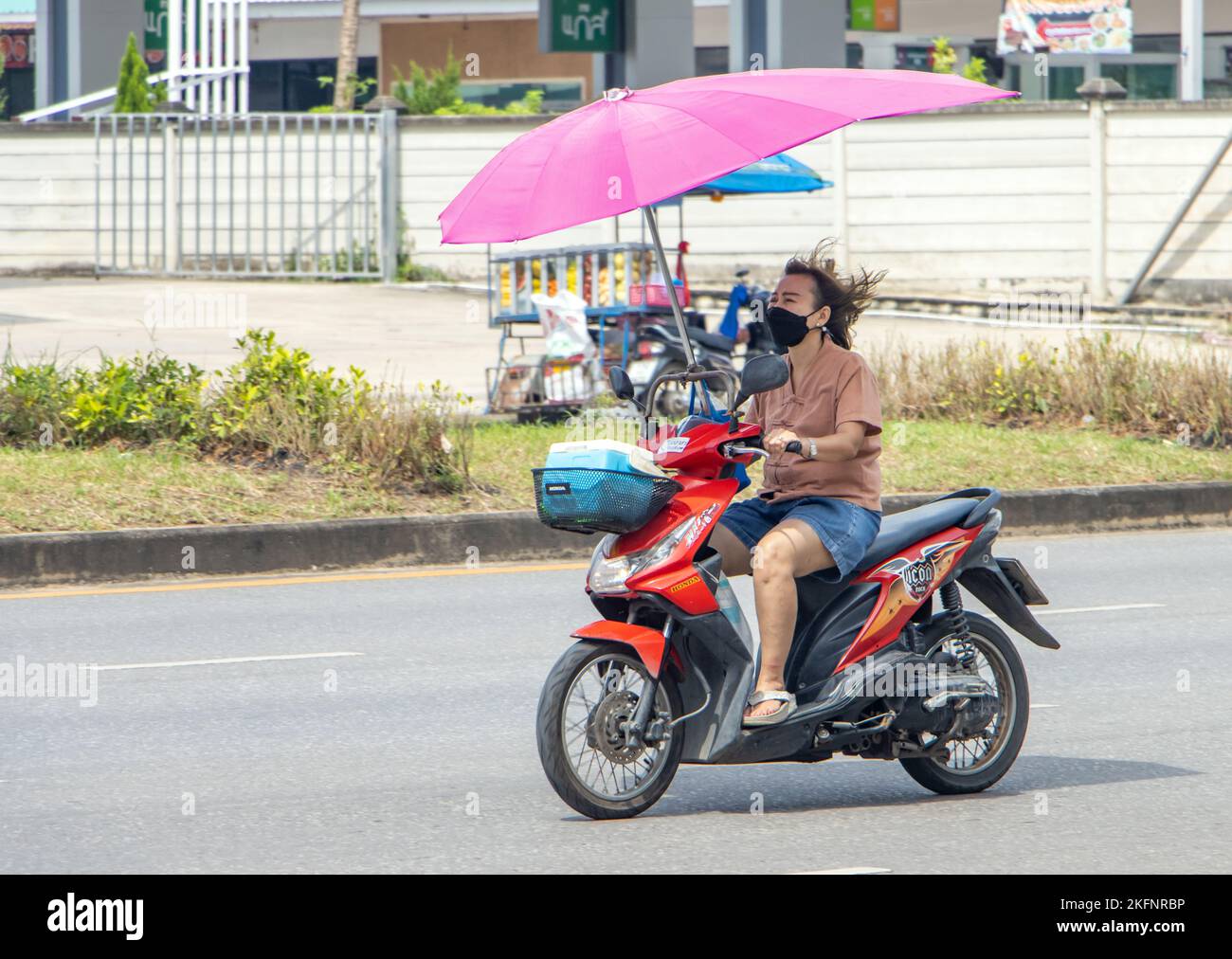 RATCHABURI, THAILAND, NOVEMBER 16 2022, Eine Frau fährt mit einem am Lenker befestigten Regenschirm ein Motorrad Stockfoto