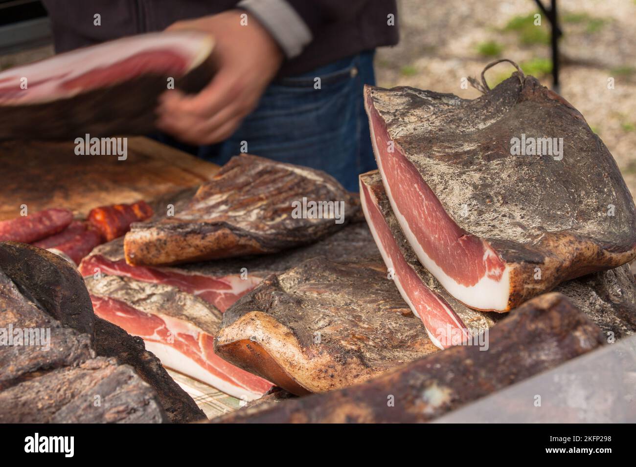 Traditionelles geräuchertes Speck, geschnitten vor Ort während einer Feier im Val di Funes, Dolomiten. Stockfoto