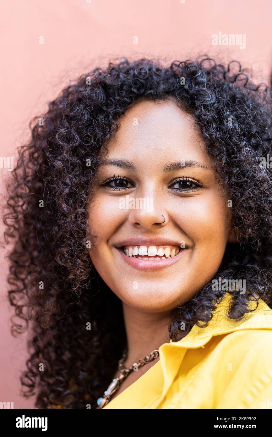 Junge südamerikanische lockige Frau lächelt vor der Kamera in der Stadt - Vertikales Porträt - Fokus auf Gesicht Stockfoto