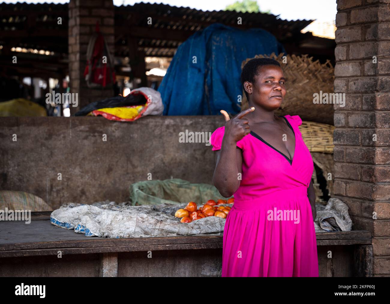 Die weibliche Marktverkäuferin in leuchtend rosa Kleidern lenkt die Aufmerksamkeit auf sich selbst, auf dem Markt in Mzuzu, Malawi. Stockfoto