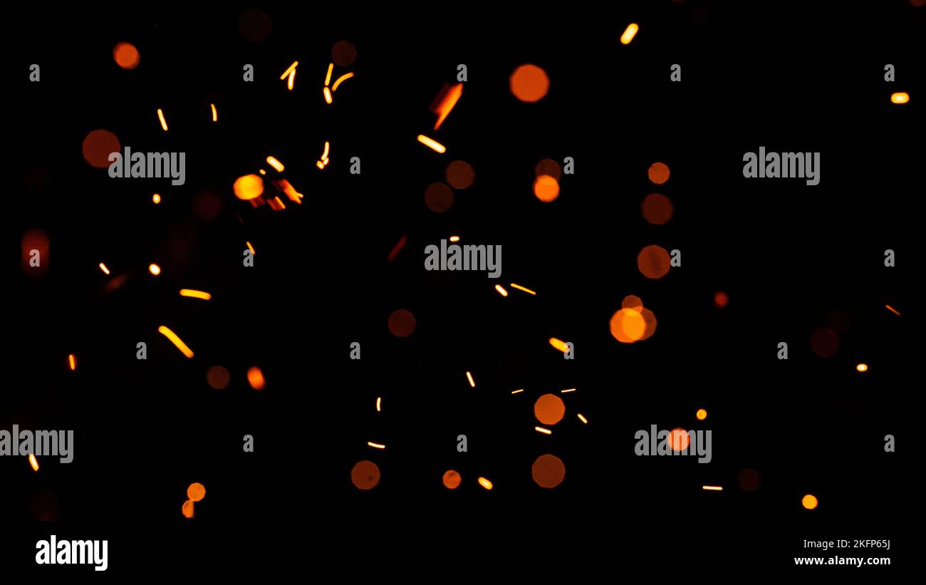 Leuchtend gelbe Funken auf schwarzem Hintergrund, gelbes helles rundes Bokeh. Partikel brennender Glut fliegen und leuchten isoliert am Nachthimmel. Stockfoto