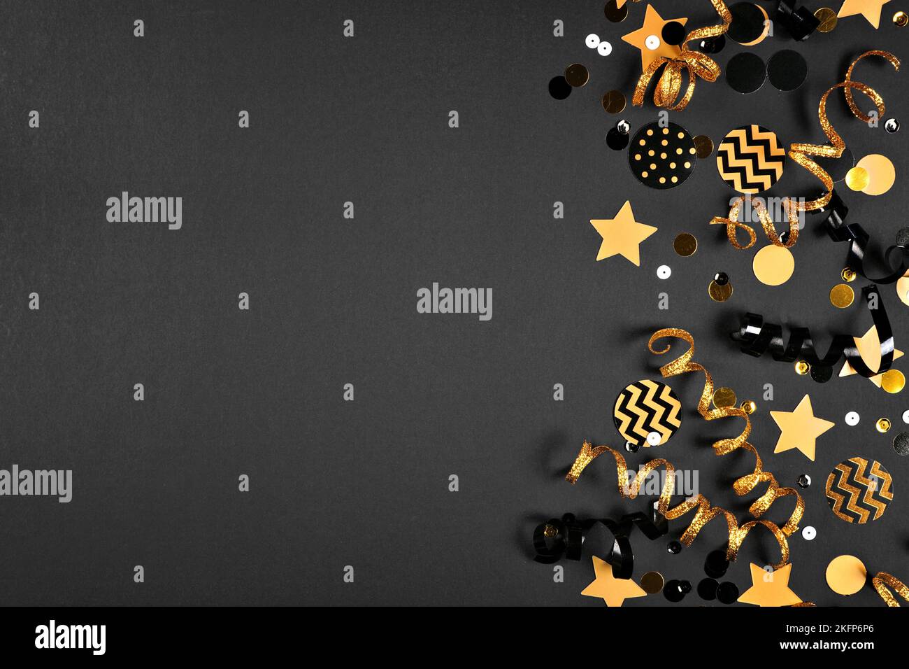 Party-Seitenrand mit glitzernden schwarzen und goldenen Bächerchen und Konfetti. Draufsicht auf schwarzem Hintergrund. Stockfoto