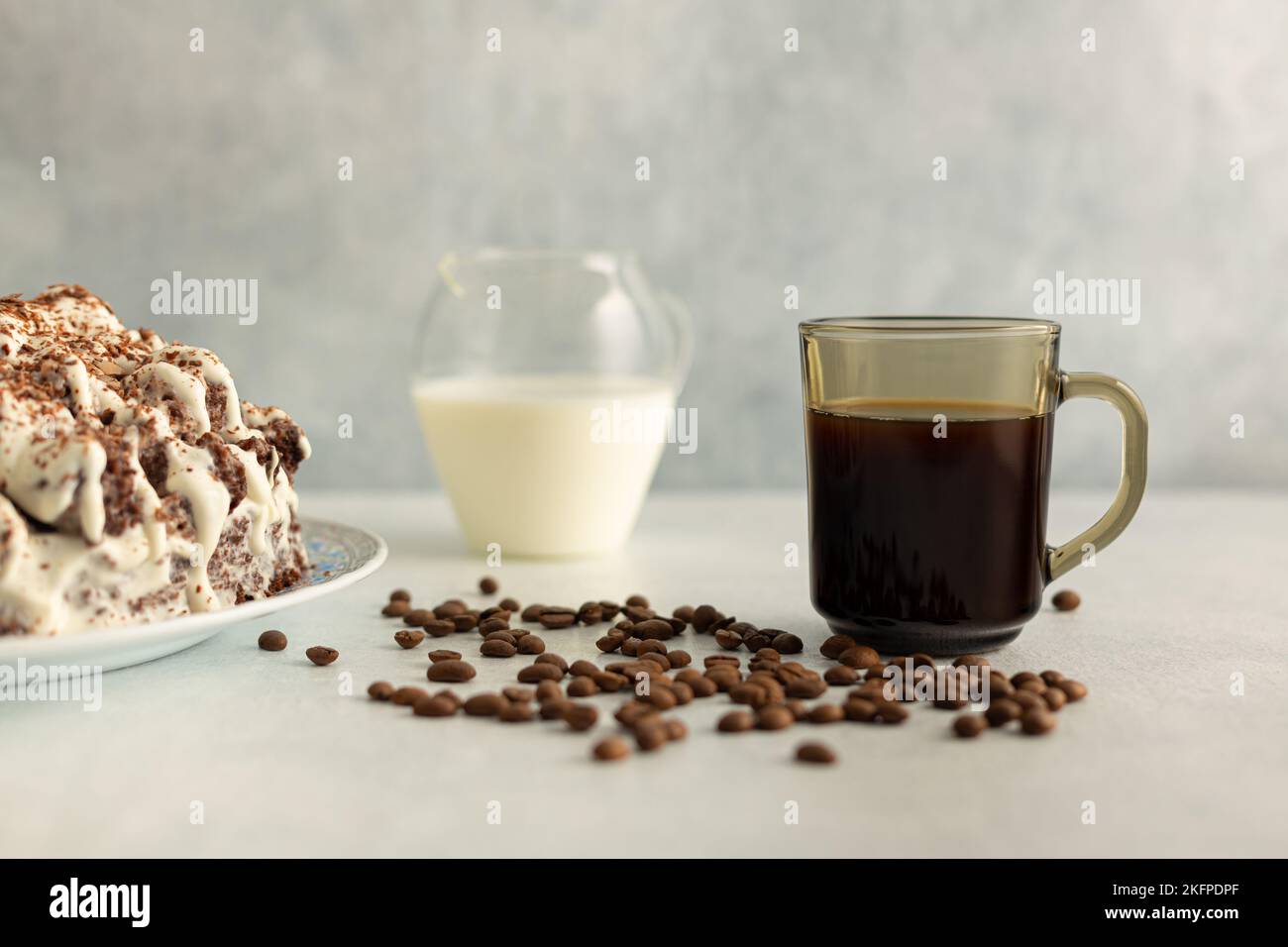 Kaffee mit Rahm in einem Glas Becher mit Kaffeebohnen, Sahnetorte. Trinken Sie auf hellgrauem Hintergrund. Stockfoto
