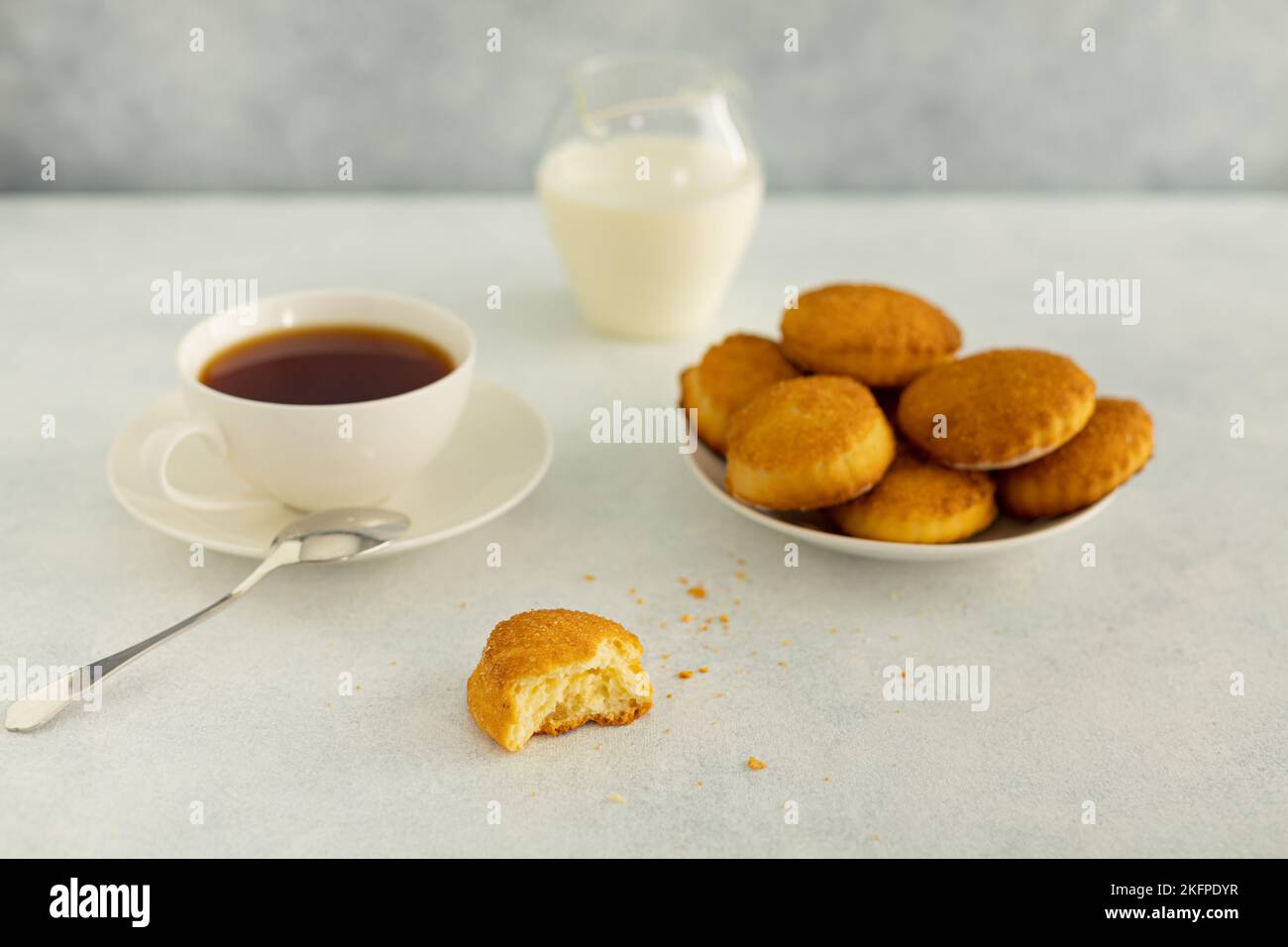 Köstlicher Snack: Eine Tasse schwarzen Tee mit Milch und ein Teller mit Keksen auf grauem Hintergrund. Stockfoto