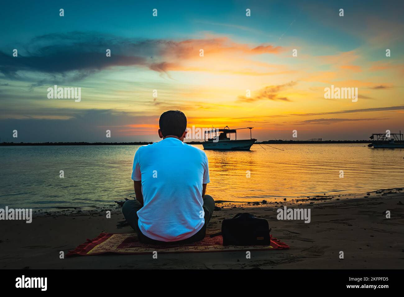 Mann, der sitzt und den Sonnenuntergang über dem Meer beobachtet. Dammam, Saudi-Arabien. Stockfoto