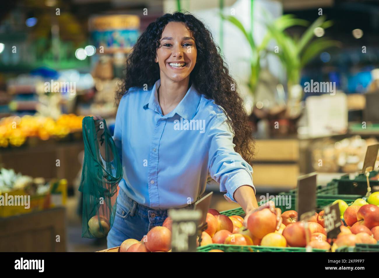Porträt einer glücklichen Frau Shopper im Supermarkt, Hispanic Frau wählt Äpfel und Früchte lächelnd und Blick auf die Kamera, mit Lebensmittelkorb wählt Waren. Stockfoto