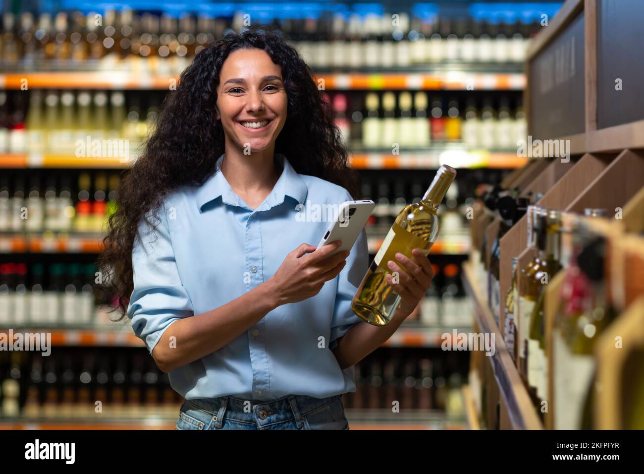Porträt einer glücklichen und lächelnden Frau, die im Supermarkt einkauft, und einer lateinamerikanischen Frau, die sich mit einer App am Telefon für Alkoholwein entscheidet, um Etiketten zu scannen und Wein zu bewerten, wobei sie lächelnd auf die Kamera blickt. Stockfoto