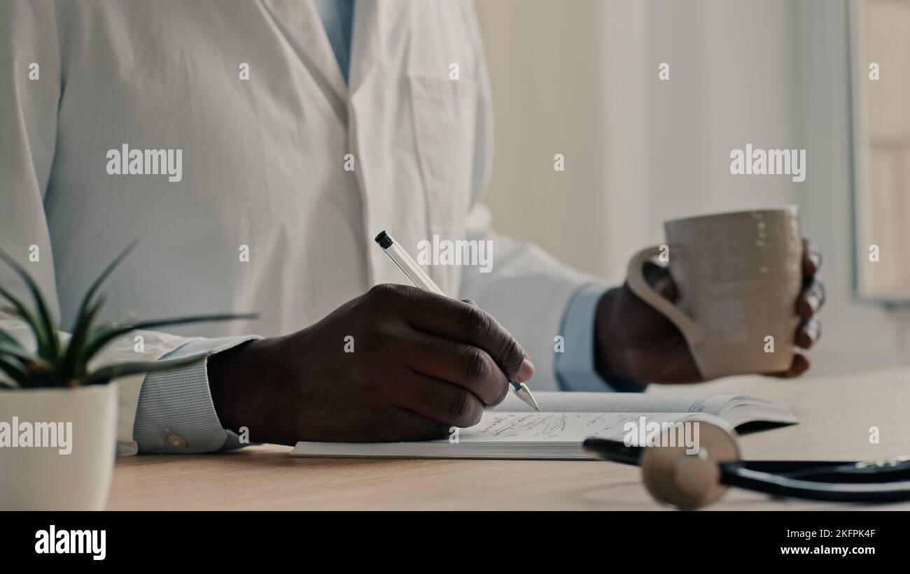 Männlicher Arzt im medizinischen Mantel sitzen in der Klinik halten Stift schreiben Rezept in Notebook afrikanischen Mann professionelle Sanitäter Hausarzt Arzt machen Stockfoto