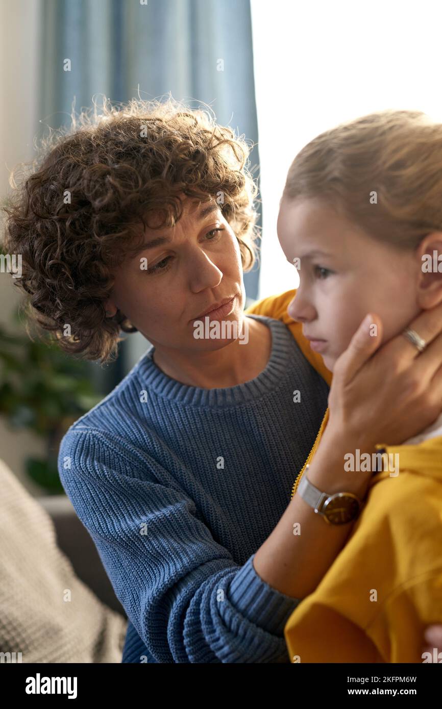 Fürsorgliche Mutter, die ihr Kind während des Gesprächs zu Hause umarmt und tröstet Stockfoto