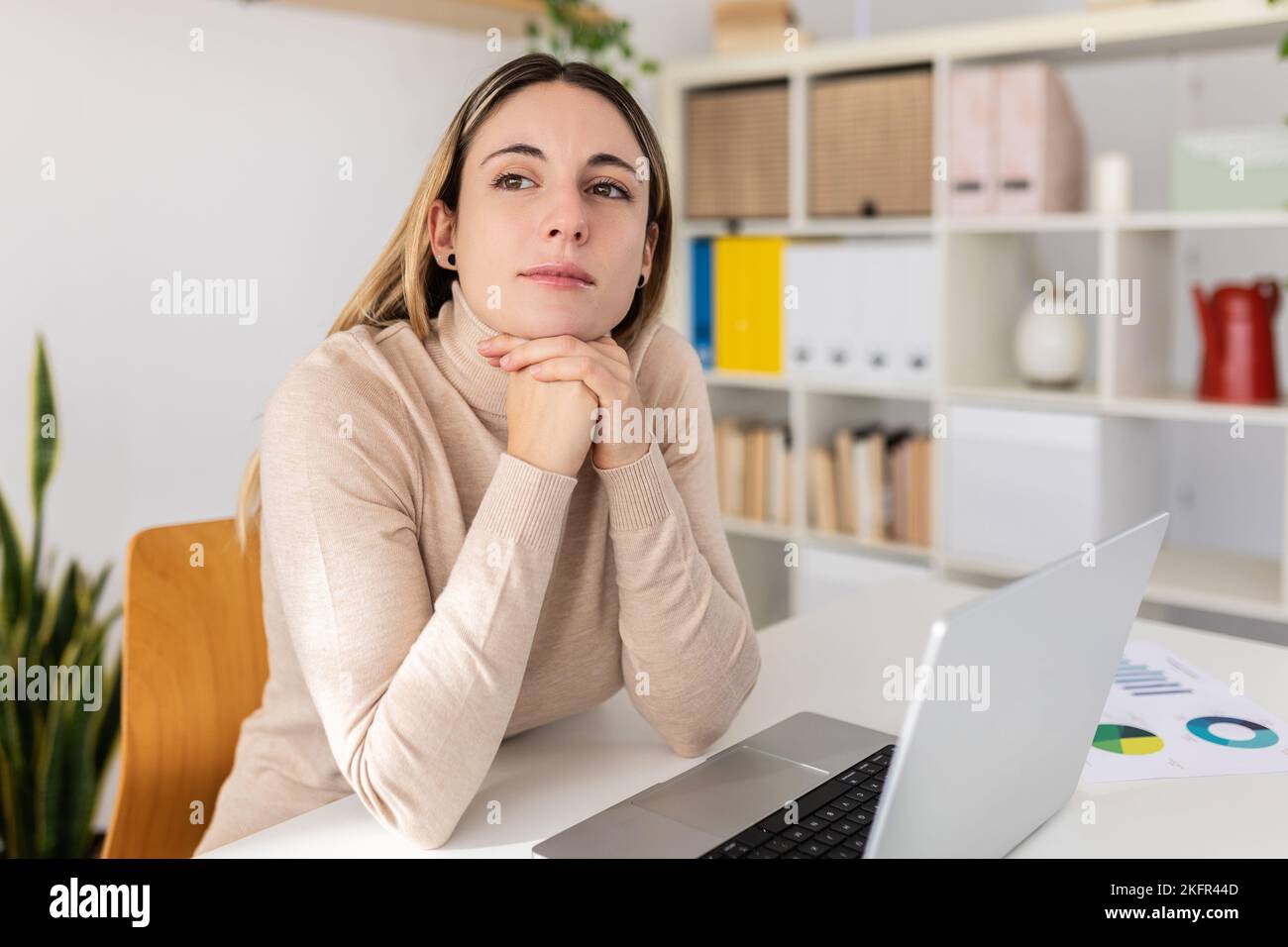 Junge Erwachsene Frau, die mit einem Laptop am Schreibtisch sitzt, denkt über Inspirationsideen nach Stockfoto
