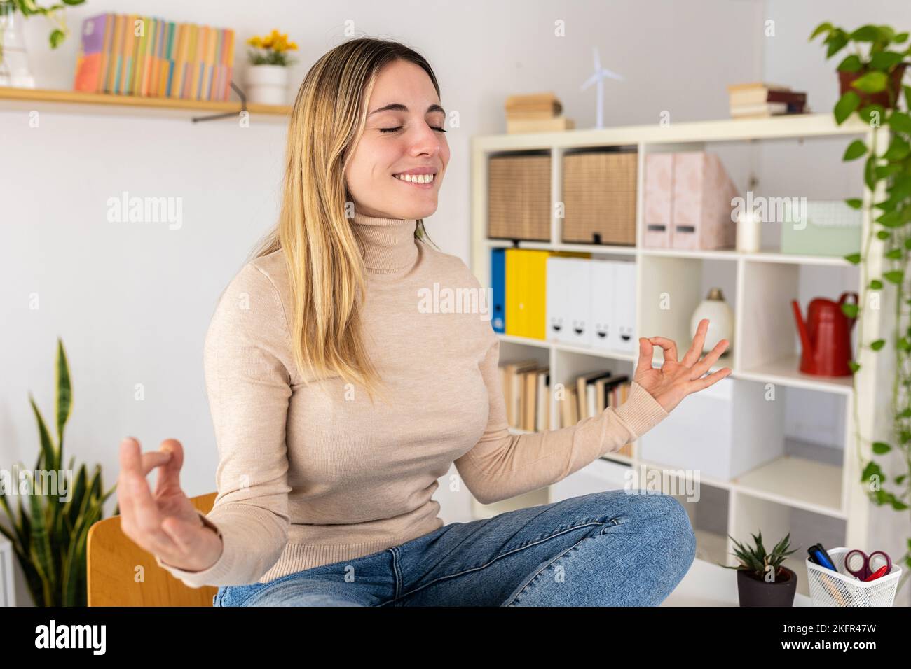 Junge Erwachsene Geschäftsfrau, die Yoga am Tisch im Heimbüro macht Stockfoto