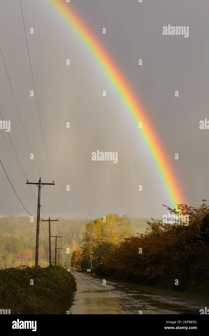 Regenbogenbogen über einer nassen Landstraße, wenn ein Regensturm vorbeizieht Stockfoto