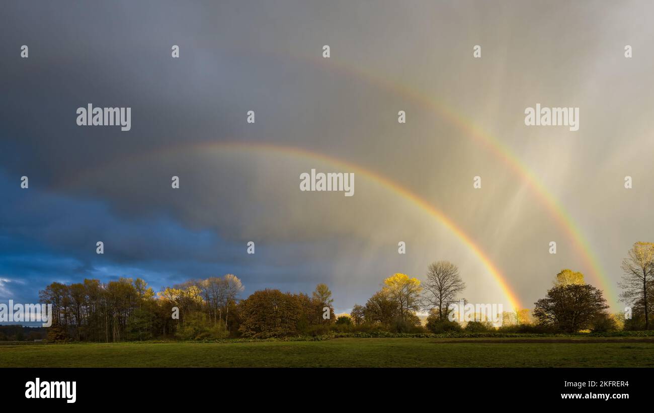Doppelter Regenbogen, der im Herbst durch Regenwellen über der ländlichen Landschaft führt Stockfoto